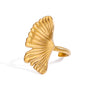 Gold tone statement ring, 18K gold plated, with a ginkgo leaf fan motif featuring crisp pleated ridges and a mirror high-polish finish, open cuff construction, no stones visible.