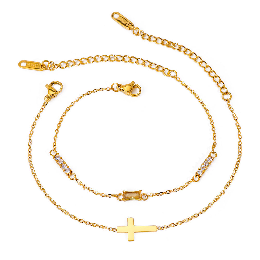 Gold tone bracelet set, 18K gold plated, with two fine cable chains featuring a cross charm and a slim bar with clear crystal accents, lobster clasps and extender chains visible.