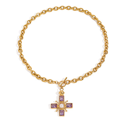 Gold tone chain charm necklace, 18K gold plated, with oval links and a toggle clasp, featuring a cross charm with lilac square crystals and a pearl center, no other stones visible.