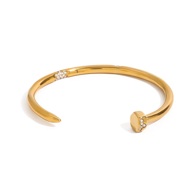 Gold tone cuff bracelet, 18K gold plated, in a nail-inspired open design with a smooth rounded band and tiny clear pavé crystal accents on the head and along the band, no other stones visible.