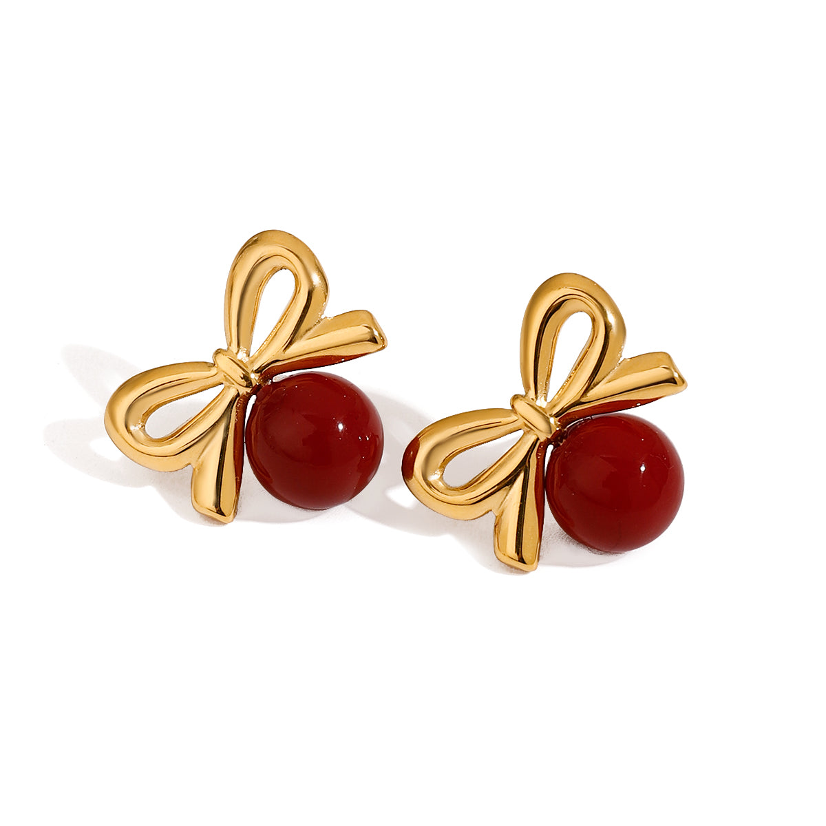 Gold tone stud earrings, 18K gold plated, shaped as bow motifs with smooth ribbon loops and a glossy red bead accent, no other stones visible, post-back not visible.